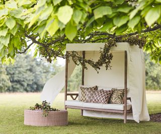 a garden day bed with a white canvas shade roof and outdoor cushions under a tree