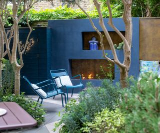 A cool blue outdoor living area with blue chairs and a fireplace area and shed