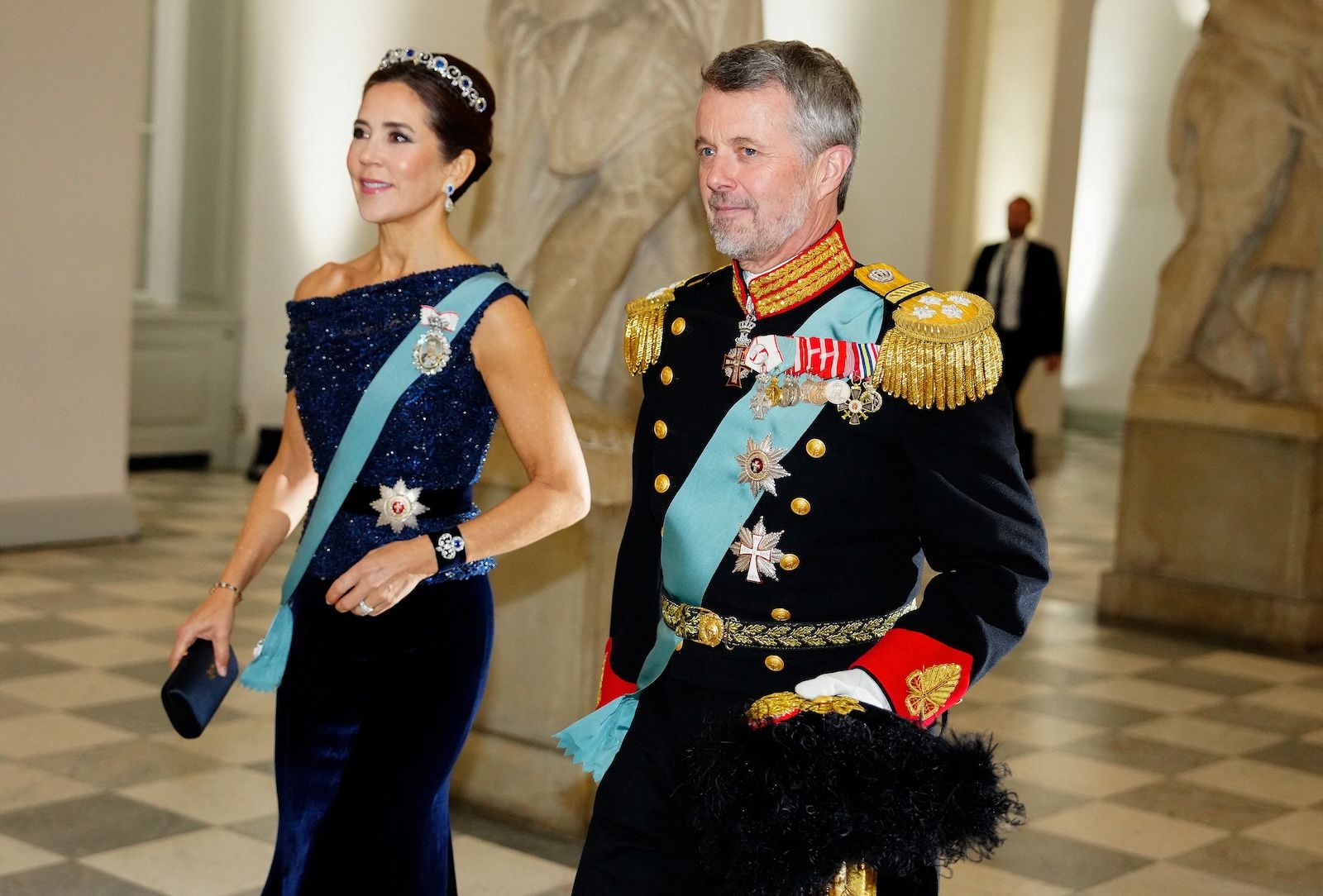 Queen Mary wearing a navy dress and tiara walking next to King Frederik of Denmark