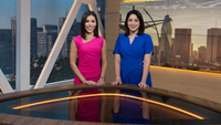 Two female anchors at a desk with city skyline in background
