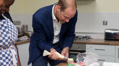 Britain's Prince William, Duke of Cambridge, (R) ices a cake during a baking class with young people and volunteers on a visit to Caius House Youth Centre in London on September 14, 2016. - The youth charity Caius House aspires to bring the local community together by helping young people bridge the educational and life skills gap between childhood and adulthood. The Duke toured Caius's facilities and met with youth who use their services