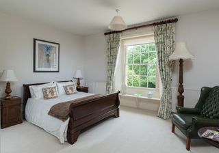 bedroom with dark oak bed frame and dark green chesterfield armchair with floor lamp