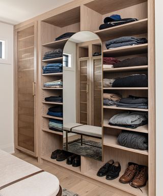 Walk in closet with jumpers stacked on shelves and a mounted mirror, Michelle Berwick Design