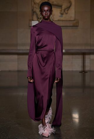 Model walking the Erdem fall 2024 runway show wearing a plum gown with a long cape with pink satin feathered pumps.