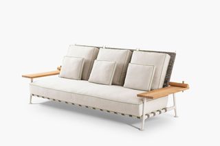 A three seat sofa with beige cushions and wooden arms rests at either end.