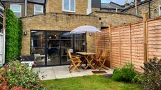 a newly built fence in the garden of an extended home with floor to ceiling glazing and a patio dining area
