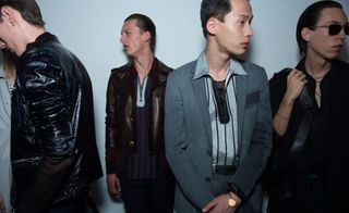 Group of male models in dark clothing standing around a studio