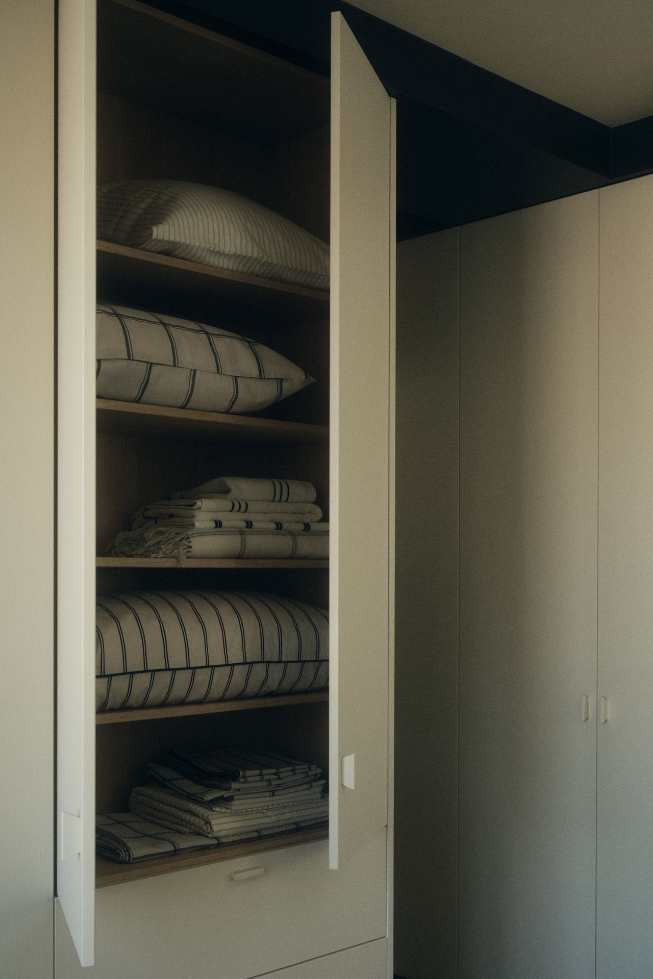 Image of a white cabinet ajar, showing white and black striped linen folded and stacked inside.