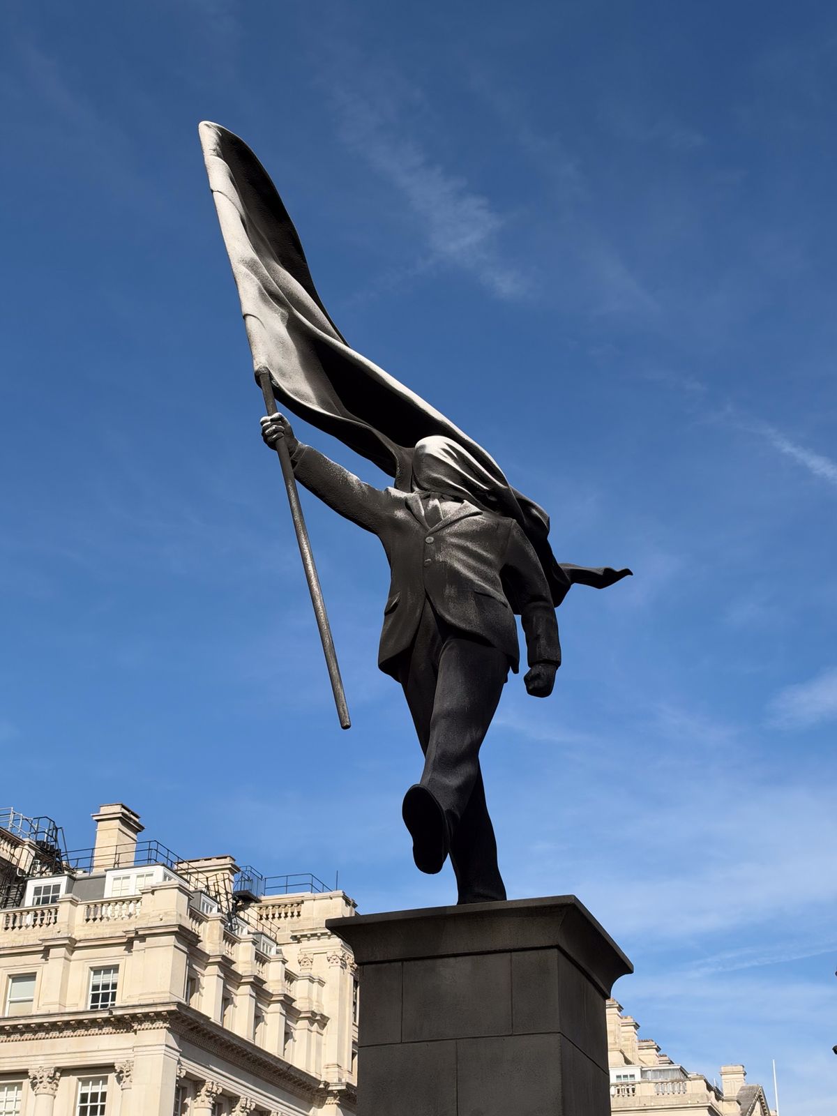 Low-angle close-up of a dark sculpture depicting a walking figure carrying a large billowing flag.