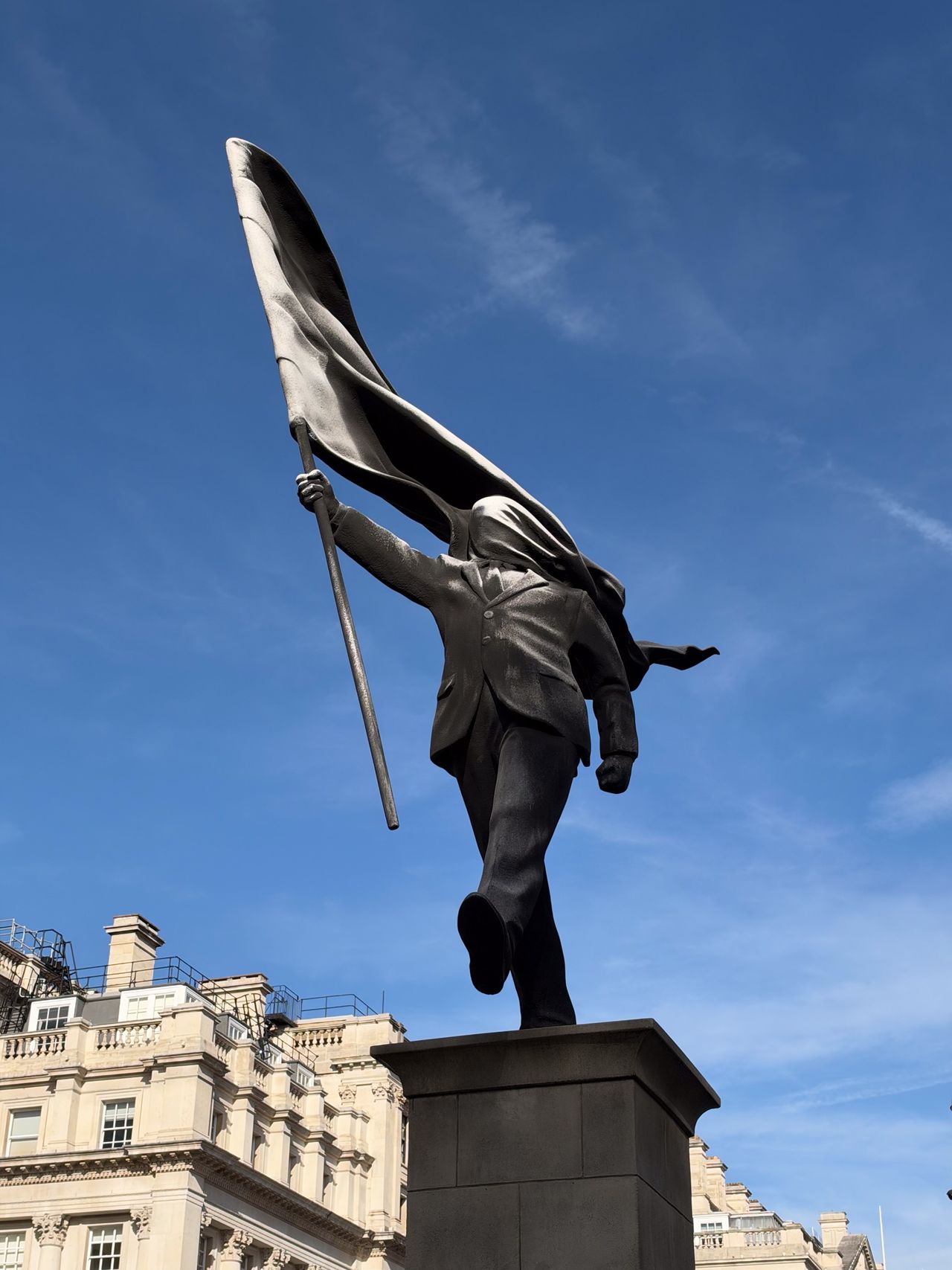 Low-angle close-up of a dark sculpture depicting a walking figure carrying a large billowing flag.