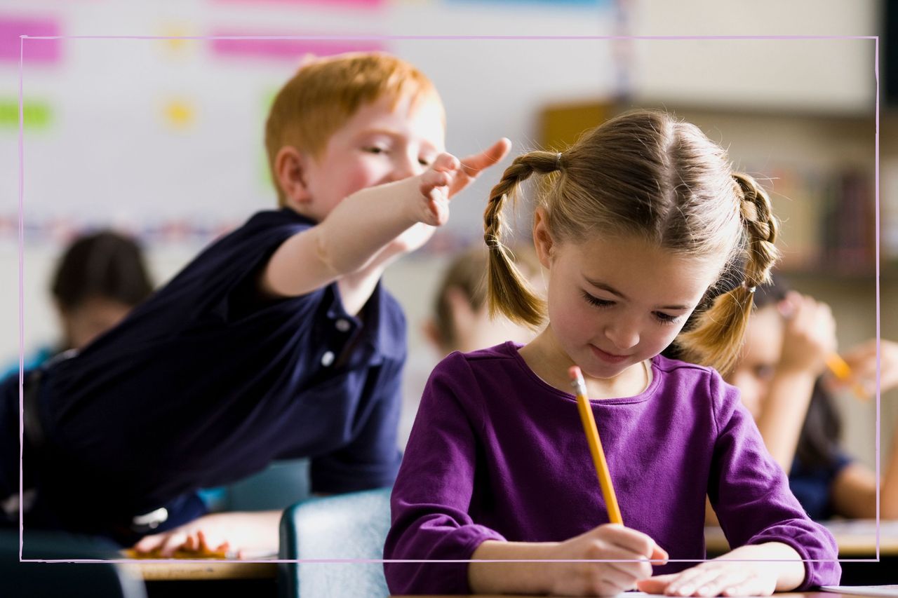 A boy in a classroom reaching forward to pull a girl&#039;s pigtail