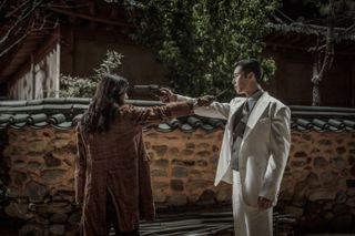two people (Han So-hee as Yoon Chae-ok, Park Seo-jun as Jang Tae-sang) aim guns at each other while standing in an alley at night, Netflix k-drama Gyeongseong Creature