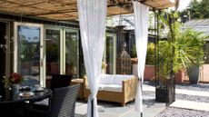 Boho-inspired covered outdoor patio featuring a dining set, loveseat, storage box, and breezy white curtains hanging overhead