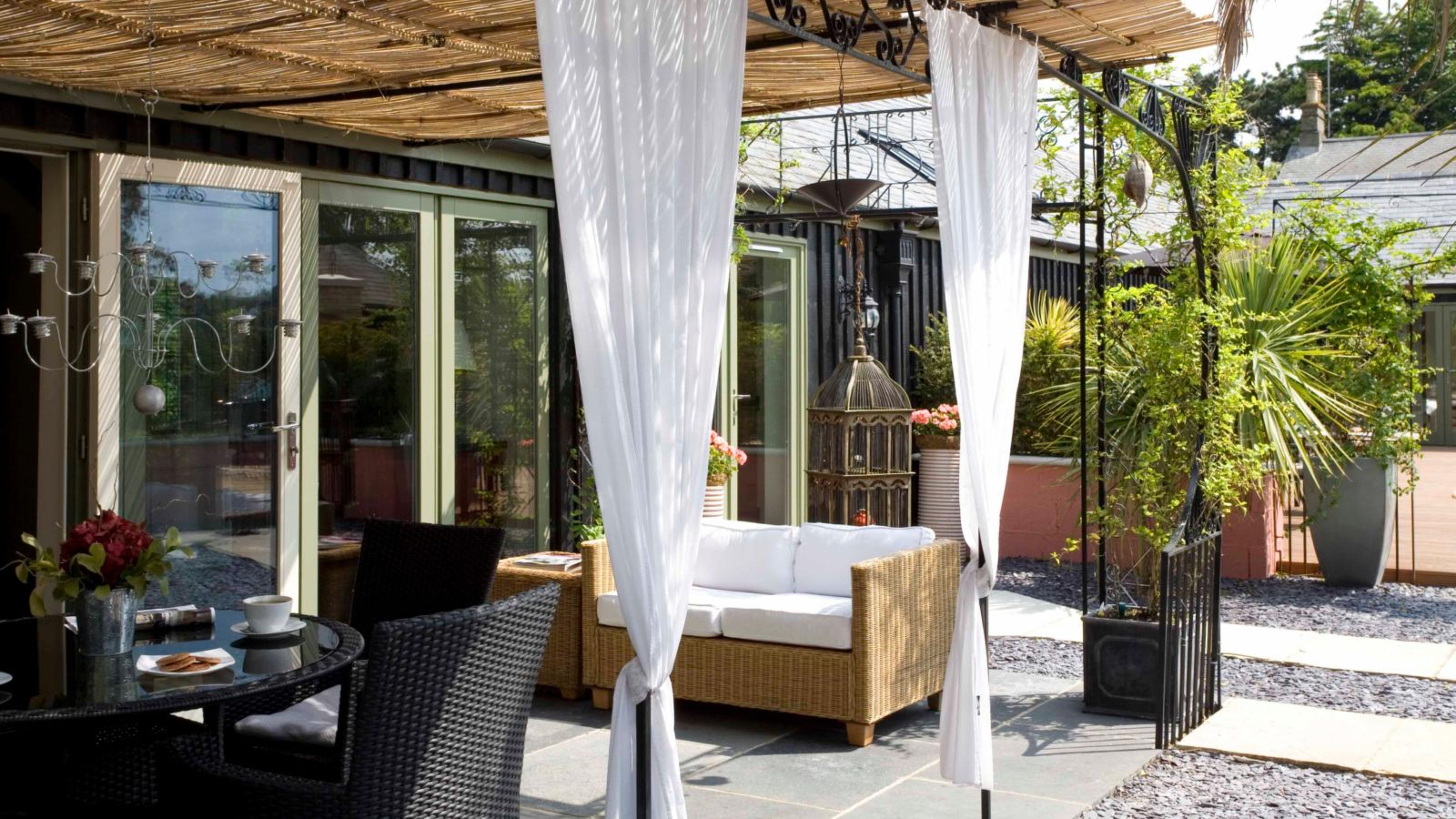 Boho-inspired covered outdoor patio featuring a dining set, loveseat, storage box, and breezy white curtains hanging overhead