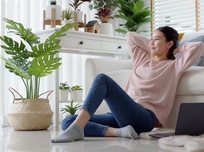 A peaceful woman sits on the floor surrounded by houseplants