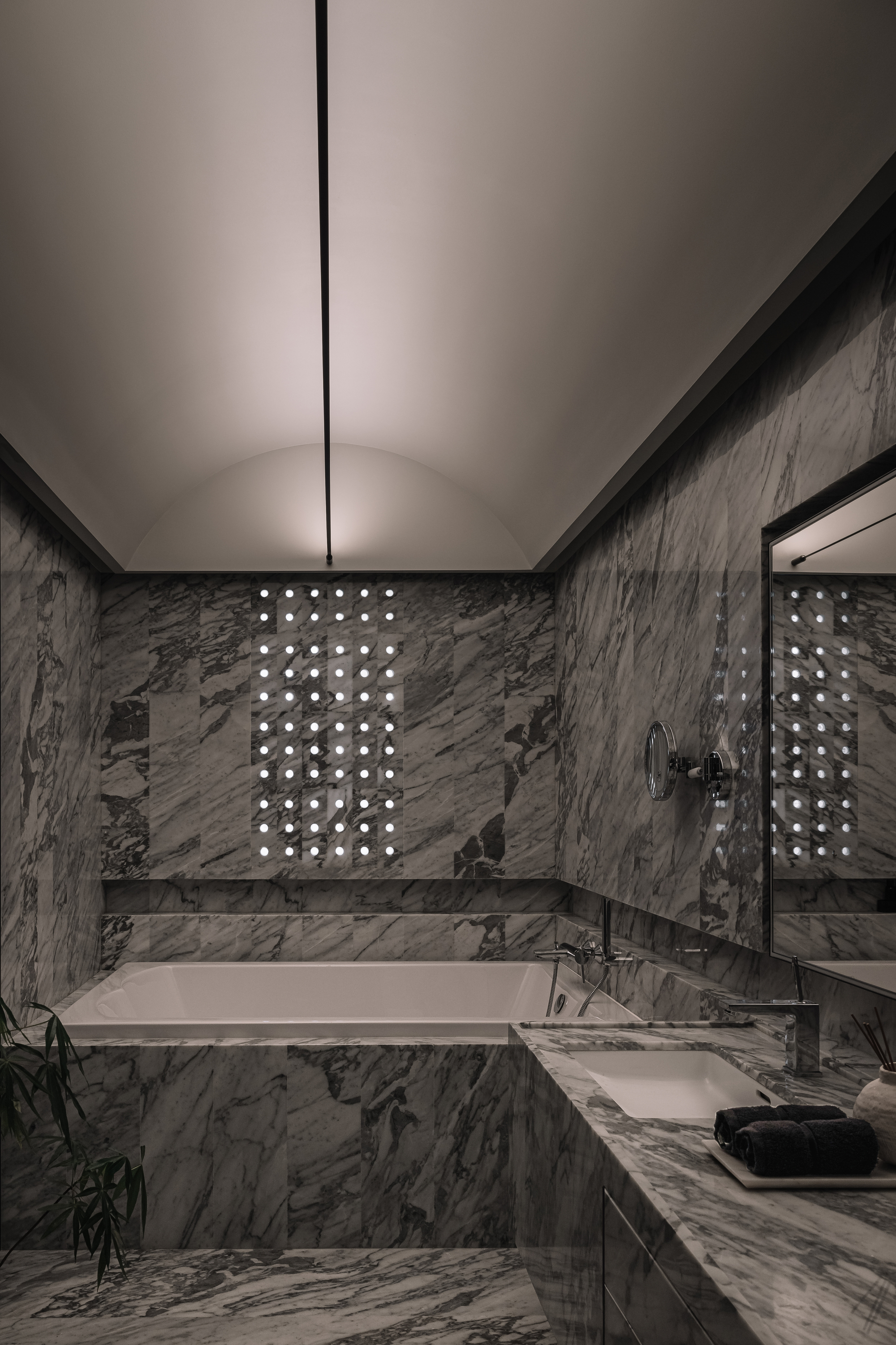 bathroom with curved ceiling, marble floors, walls, and counter, with built-in bath, and perforated holes as the window