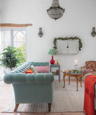 white painted living room with arched windows, velvet chesterfield style sofa, and crystal chandelier and wall lights