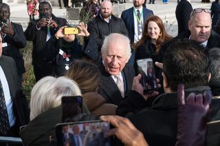 King Charles standing outside in a crowd of people with their phones up taking photos of him