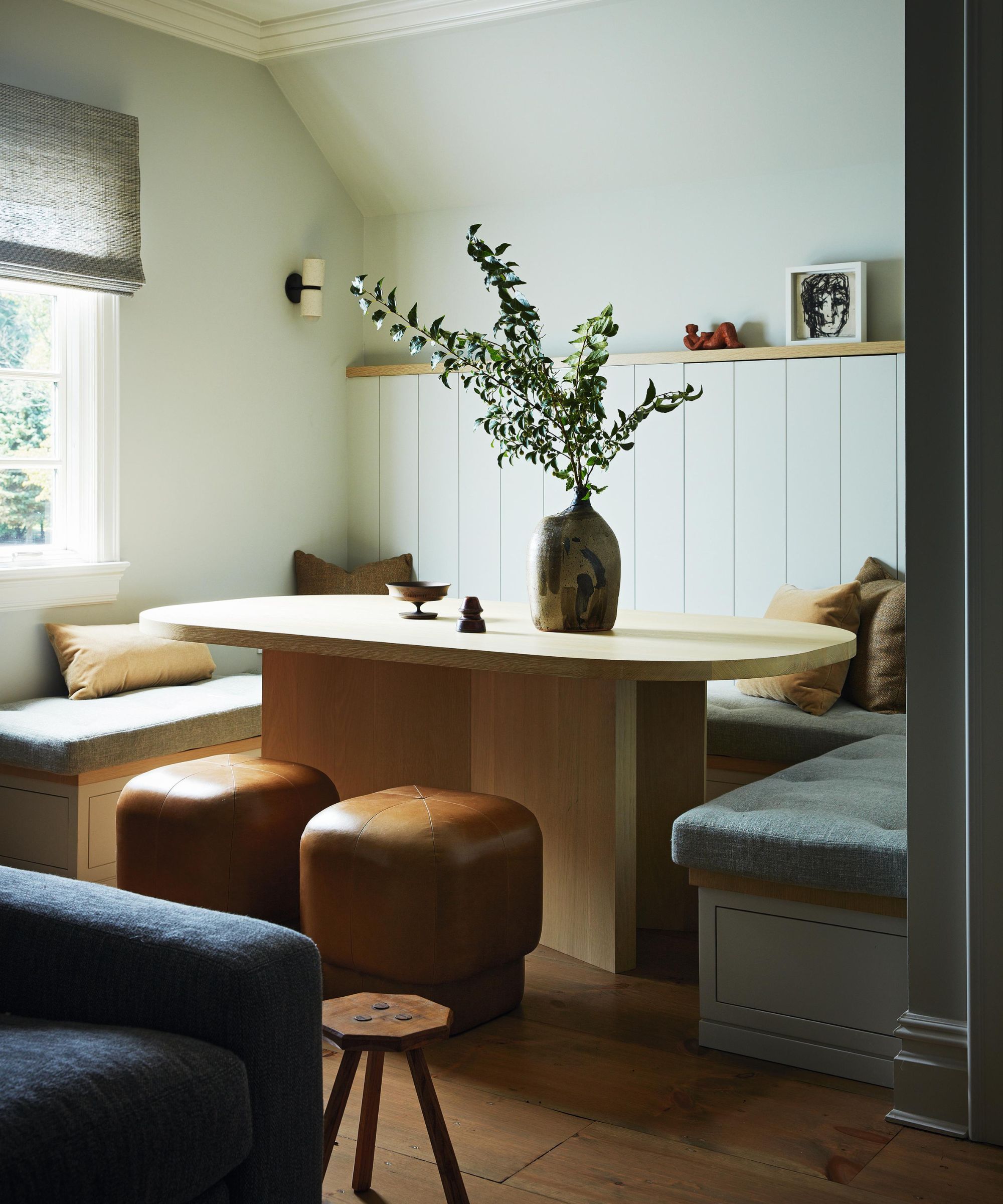 a small banquette dining area in a kitchenette with leather stools, paneled walls, and a light oak curved table