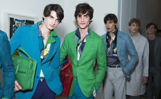 Three male models wearing clothing by Berluti in green and blue shades.