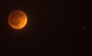 the moon appears red beside a bright blue star in the sky