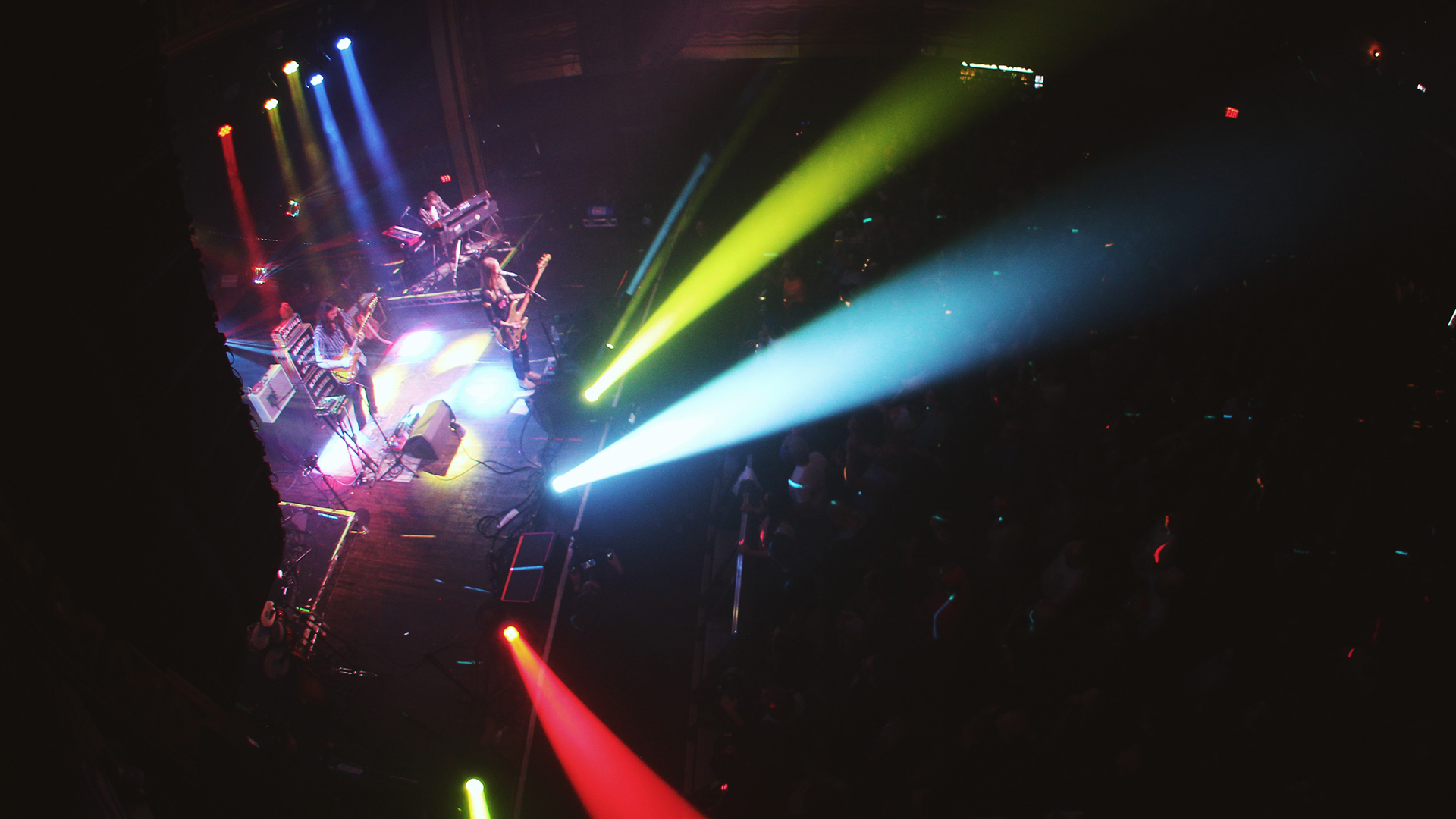 a rock band on stage in a crowded night club full of multicolored lights