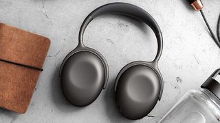 KEF Mu7 headphones facedown on a table top alongside a small suede-covered book and a glass water bottle