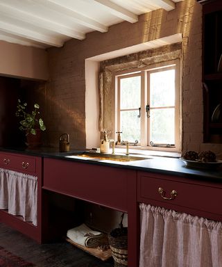 Red painted cupboard and brass sink in a kitchen by deVOL