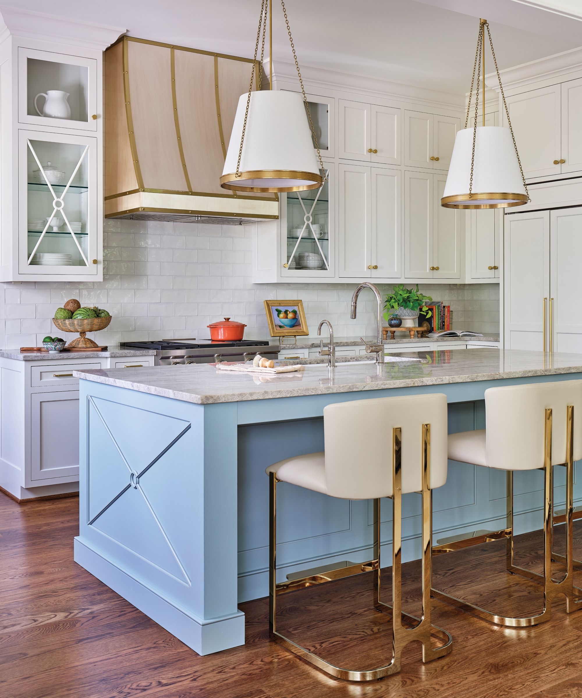 A kitchen with white perimeter cabinets, a light blue island, and brass details