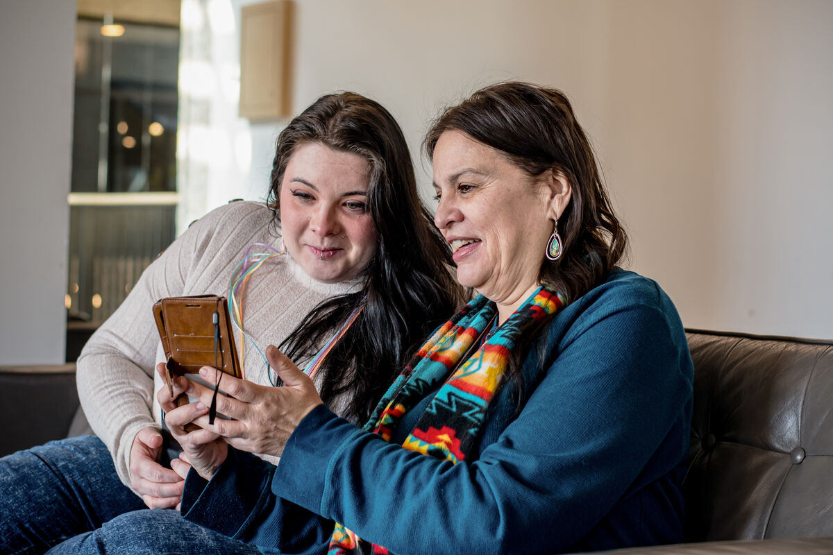 In a scene of mutual fascination, an indigenous mother and daughter bond over an intriguing discovery on a phone screen, deepening their connection through shared curiosity.