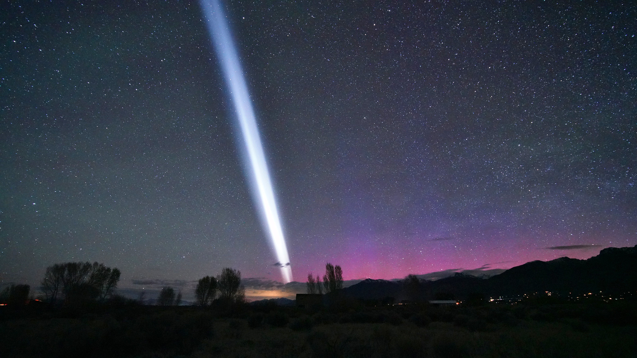 a bright white streak splits the starry sky with purple and pink auroras shining below.
