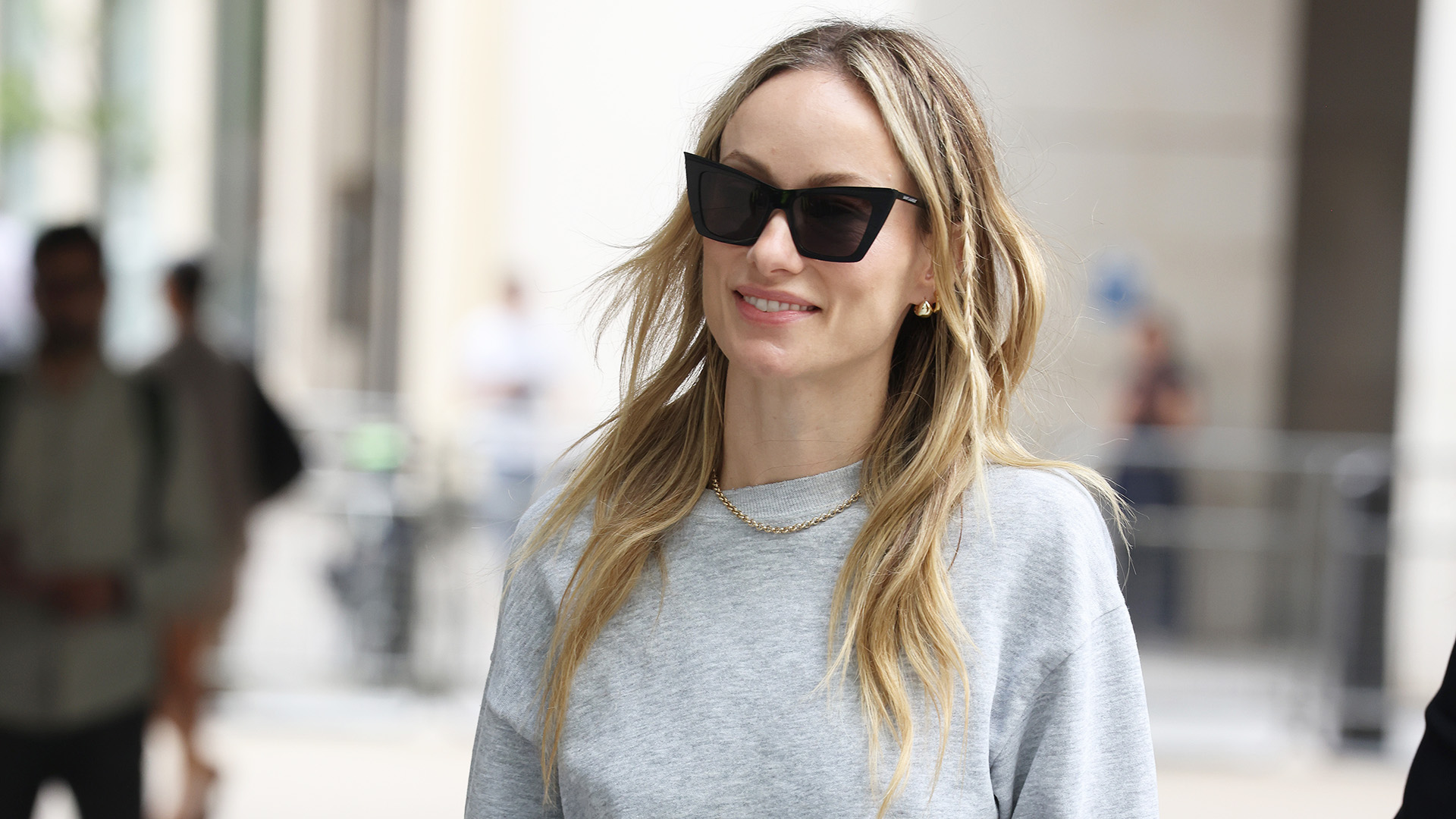 Olivia Wilde wearing a gray sweatshirt, satin knee-length skirt, and ruched loafers in London