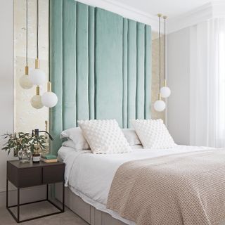 A couples' bedroom with teal coloured headboard decor and white/brass pendant lights with large bed and houseplant decor