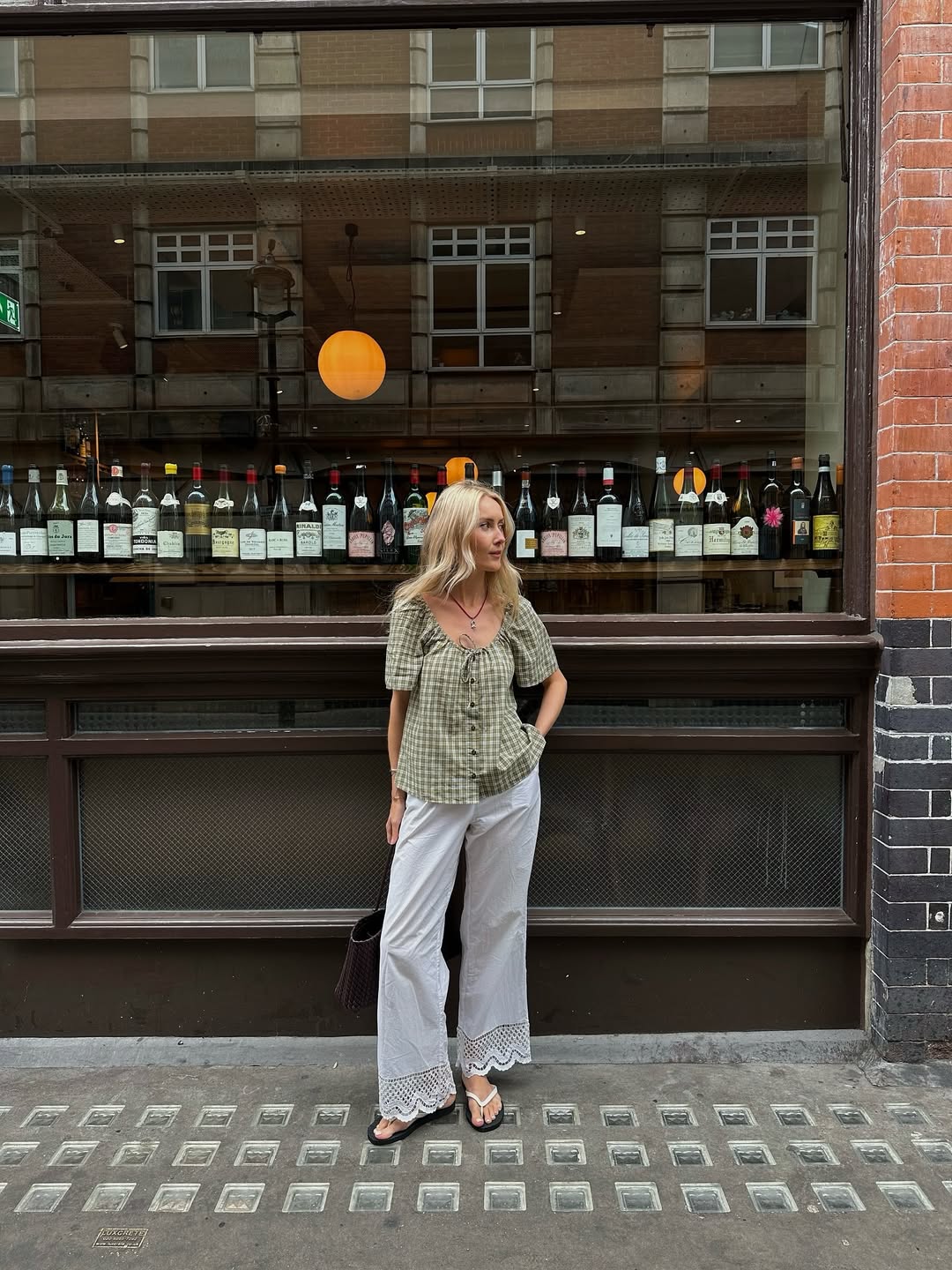 @chloekathbutler wears a gingham blouse, white trousers, brown woven tote and white contrast flip-flops