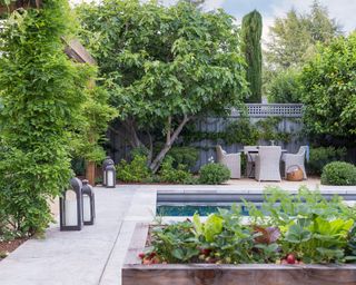 An example of backyard ideas with a pool showing pool landscaping using lanterns, raised beds and outdoor furniture