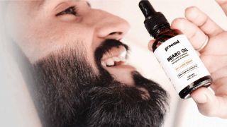 A bearded man smiling while holding beard oil