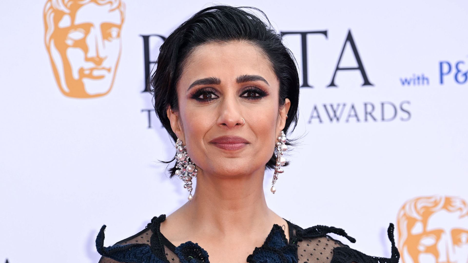Anita Rani pictured at the TV BAFTA awards in a black embellished dress with large pearl earrings, slicked back hair and a smoky eye makeup look