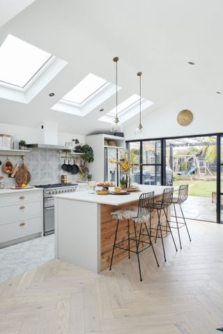 Extended kitchen with rooflights, Crittall-style door, herringbone wood floor, white kitchen and island with wooden panelling