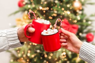 a christmas drink with a peppermint candy cane and a christmas tree in the background served in red mugs