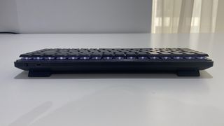 Logitech MX Mechanical Mini ligger på ett vitt skrivbord, sett från ena långsidan av tangentbordet.