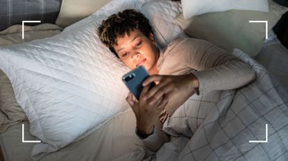 Woman lying in bed looking at a bright phone screen, trying to work out the best time to sleep and wake up