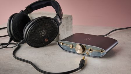 The Sennheiser HD 660S2 leaning against a concrete block next to the iFi Zen DAC 3, with the wire not plugged in.