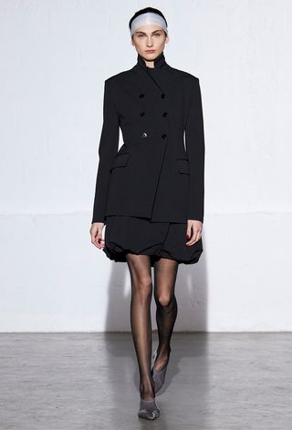 a model on the tibi fall runway with a black ballon skirt styled with a black blazer and tights and satin pointed shoes