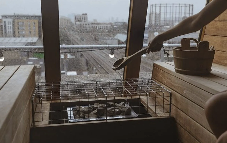 an image of someone adding water with a wooden spoon to the hot stones in the sauna