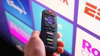 Roku remote in front of a TV running Roku OS