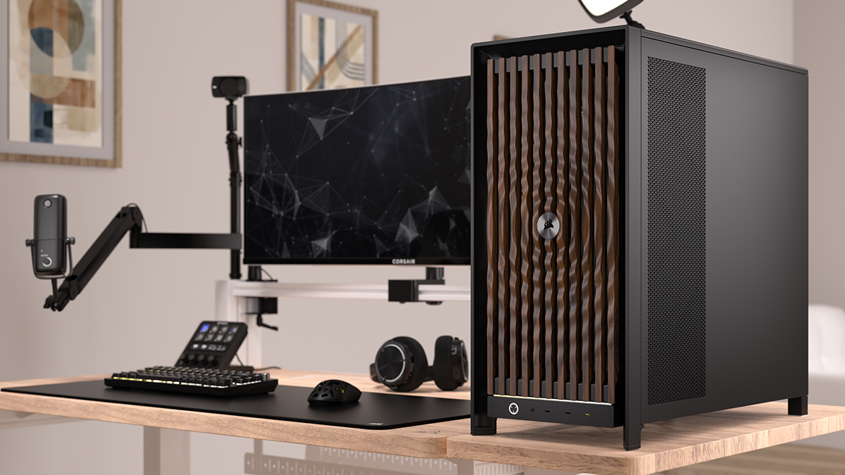 Corsair Frame 5000D (in black) with wooden ripple front panel on a desk, next gaming accessories and a monitor