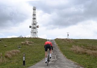 Cyclist Simon Warren climbing towards a telephone mast on top of a British hill