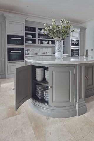 A curved gray kitchen island with an open cabinet showing stored crockery