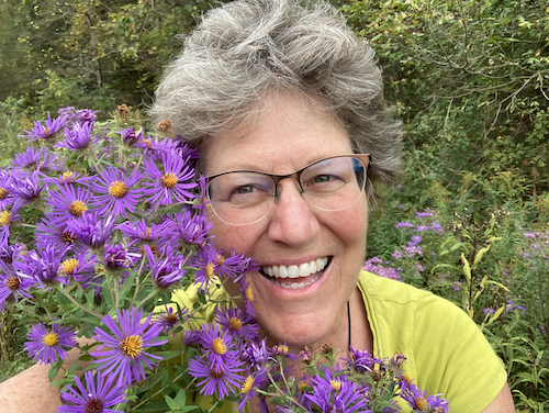 woman with grey hair smiling and holding purple flowers