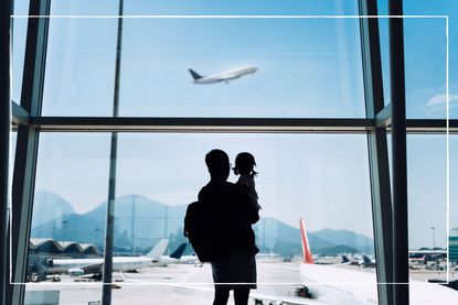 silhouette of parent and child looking out of airport window at plane taking off